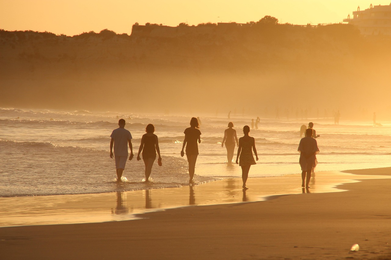 Original photo of people walking along the shoreline of a beach at sunset, backlit against golden haze